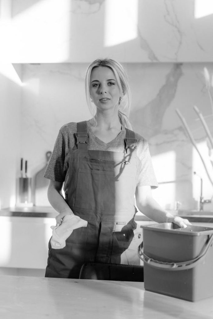 a woman in overalls holding a bucket and a rag